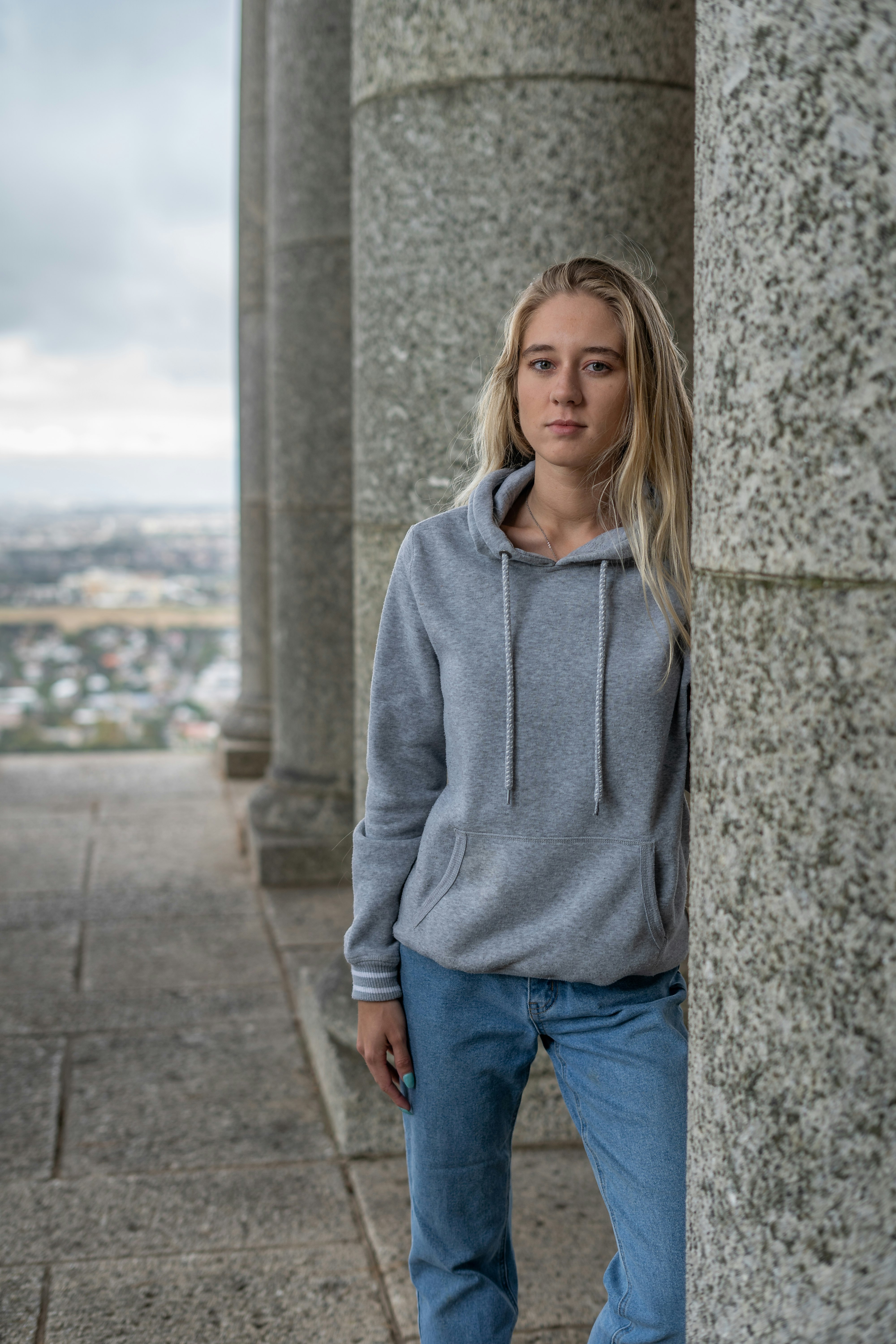 woman in gray hoodie standing beside gray concrete wall during daytime